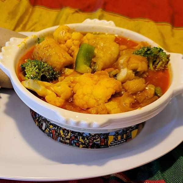 Ethiopian vegetable stew with cauliflower and broccoli in a white bowl on a colorful patterned base.
