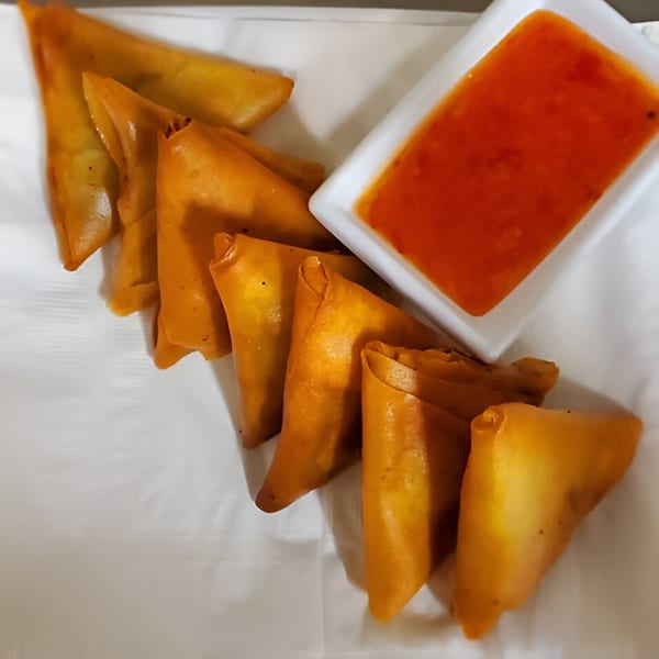 Golden-brown Ethiopian sambusas arranged on a white plate with a side of red dipping sauce.