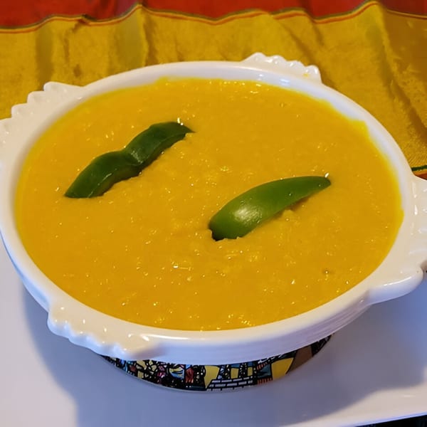 A white bowl of bright yellow Ethiopian misir wot, garnished with two green leaves, on a colorful placemat.