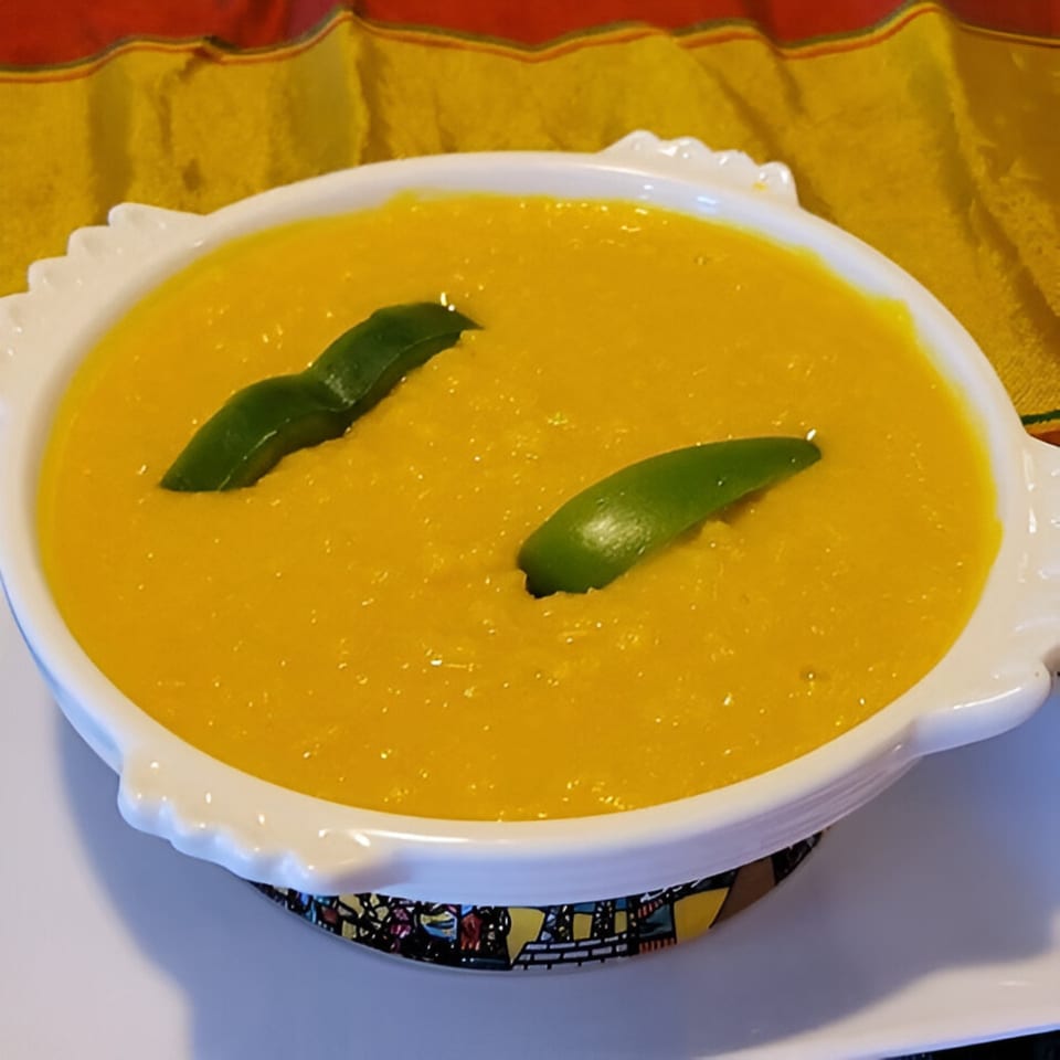 A white bowl of bright yellow Ethiopian misir wot, garnished with two green leaves, on a colorful placemat.